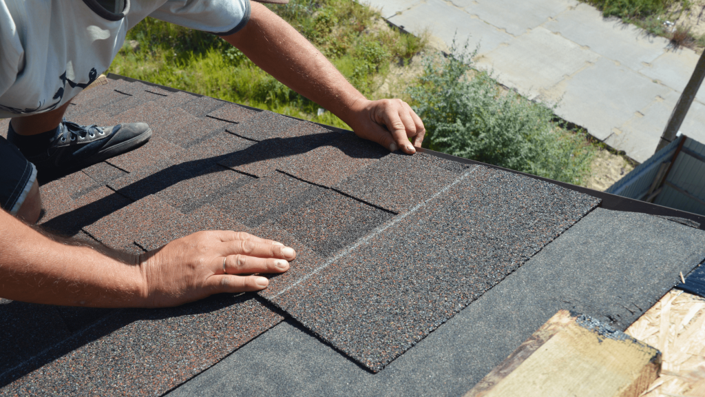 A person installing asphalt shingles on a roof, focusing on aligning and securing the shingles properly.