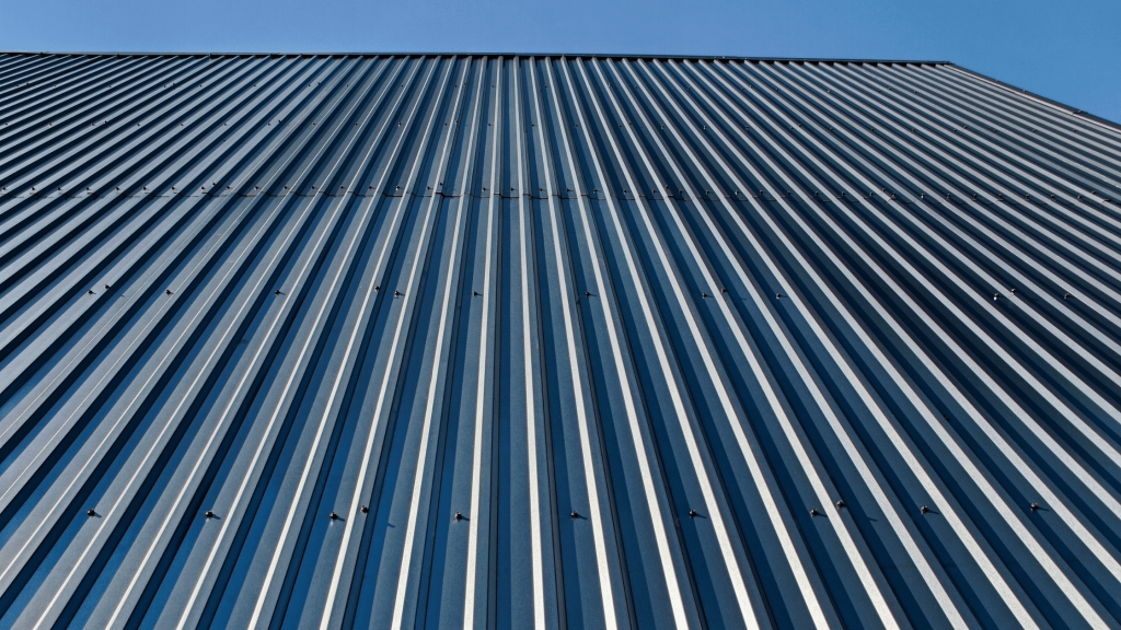 Close-up view of a large metal roof with a modern, ribbed design and metallic finish under a clear blue sky.