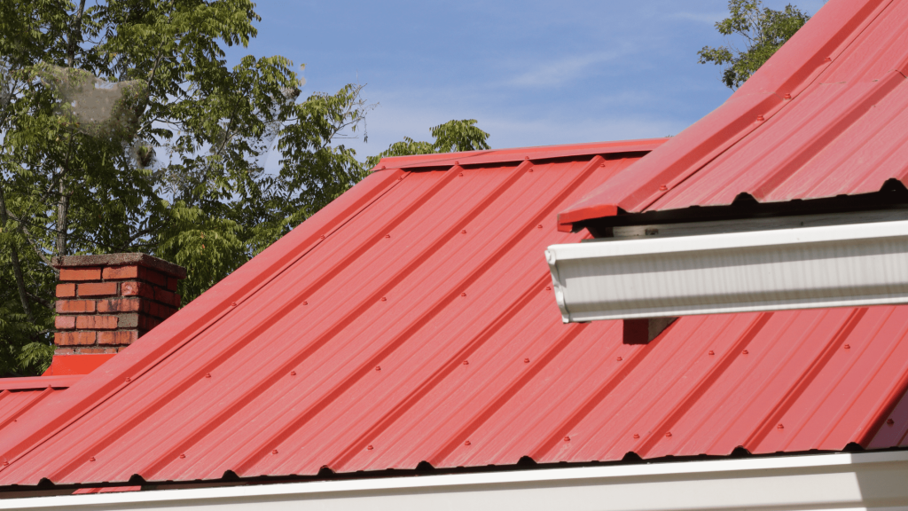 A vibrant red metal roof on a residential home with trees in the background, highlighting the durability and aesthetic appeal of metal roofing.