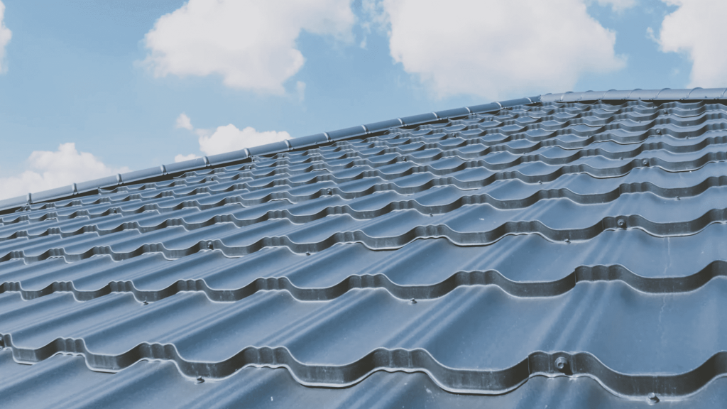 Close-up view of a blue metal roof with a textured, wavy pattern under a clear sky with scattered clouds.