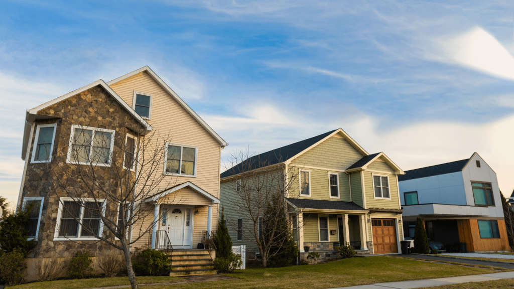 A row of three modern houses with different architectural styles, set against a clear blue sky, showcasing residential homes in a suburban neighborhood.