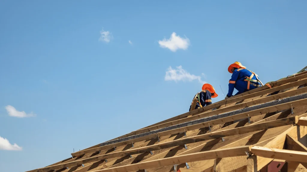Two professional roofers working on affordable roofing solutions in Asheville, NC, against a clear blue sky, ensuring quality and durability.