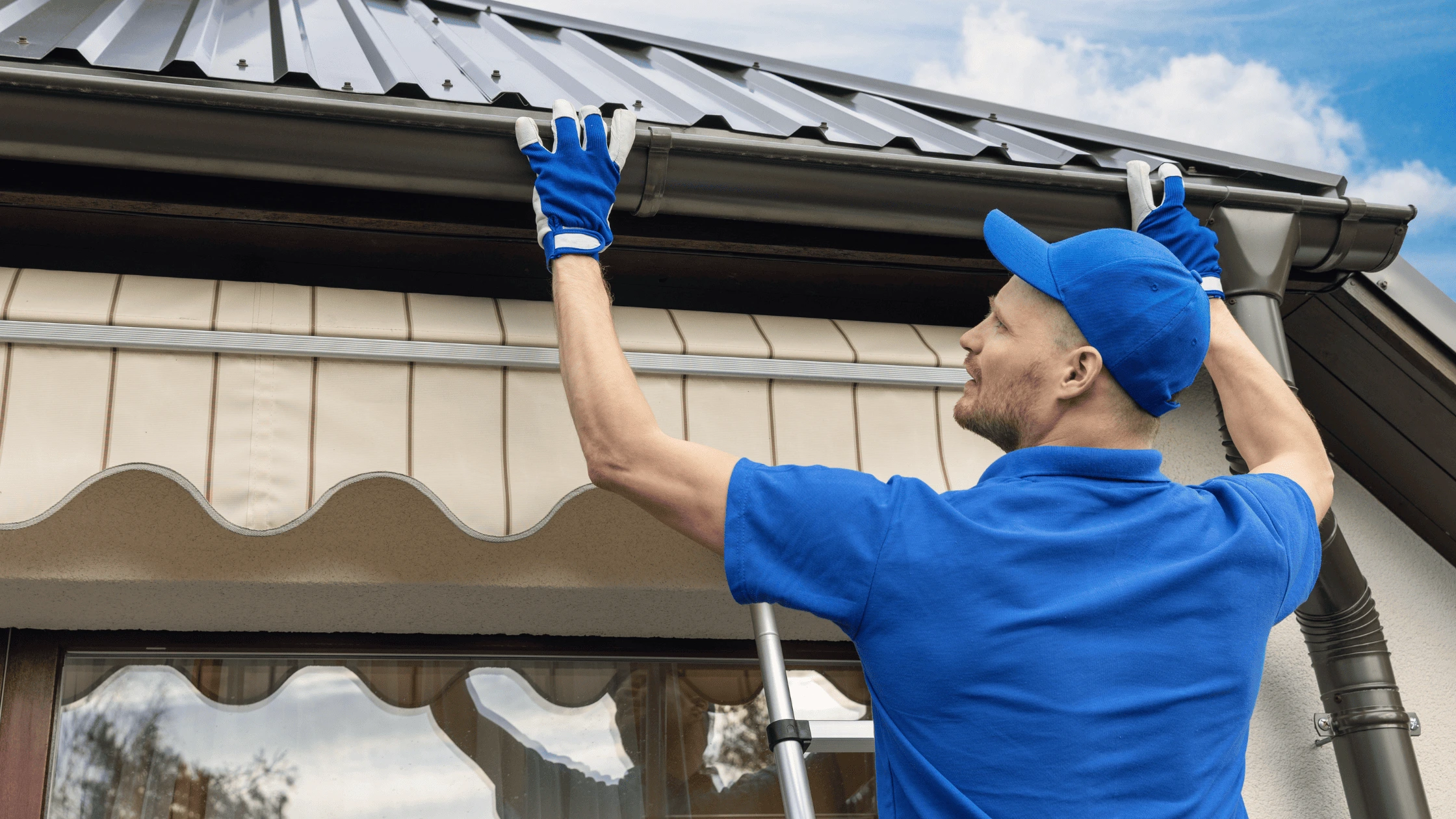 Roof repair and maintenance in Asheville, showing a professional inspecting and maintaining gutters on a metal roof.