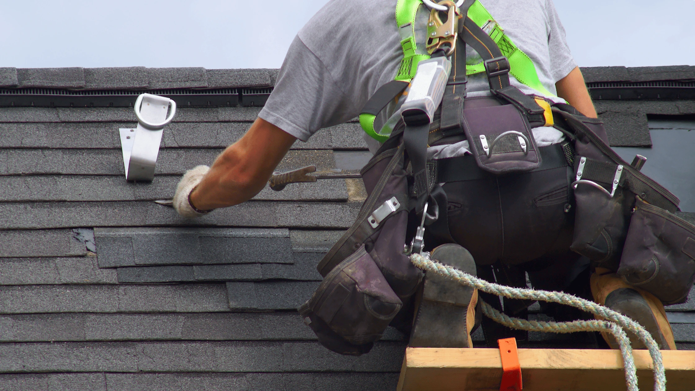 Roofer replacing shingles on sloped roof using safety harness in Asheville