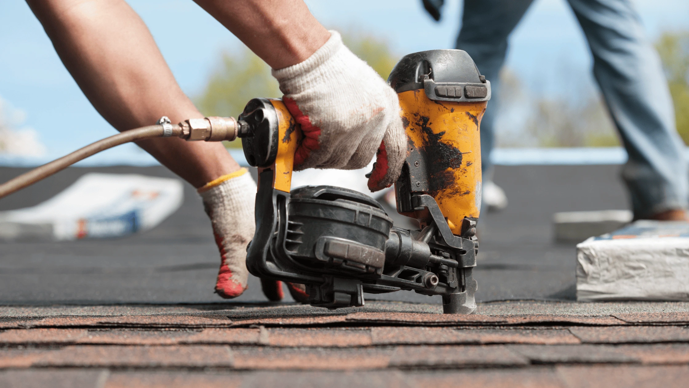 Roofer using pneumatic nail gun to install asphalt shingles on residential roof for long-lasting protection.